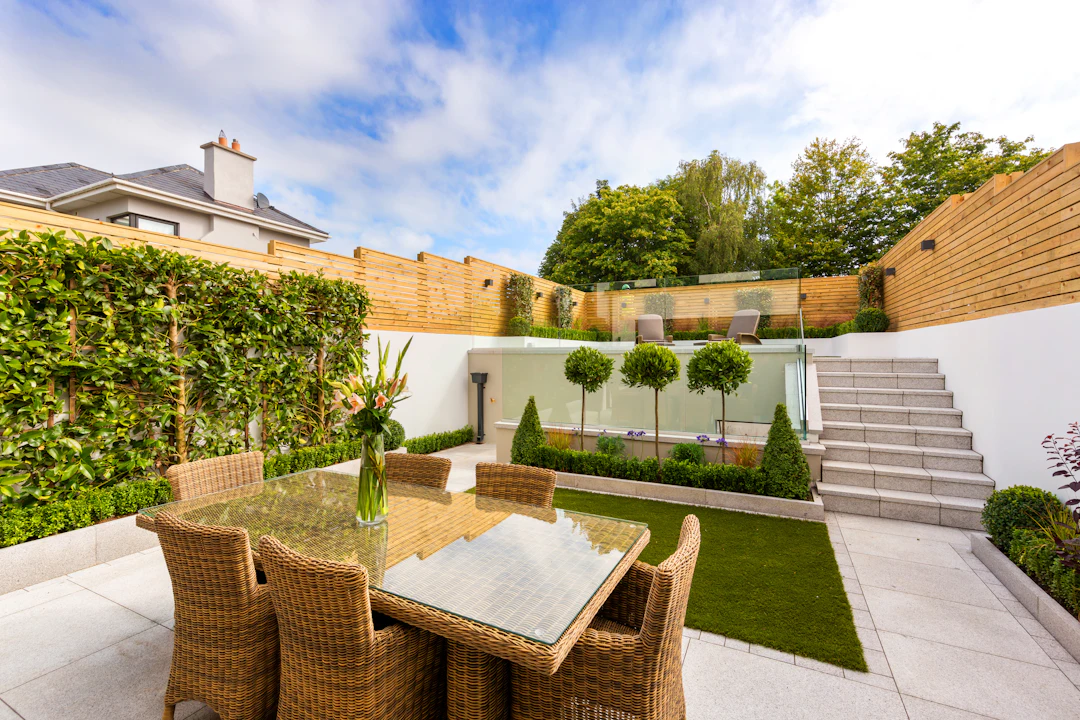 Gepflegte Terrasse mit Sitzgruppe, Rasen und Formgehölzen hinter einem Wohnhaus